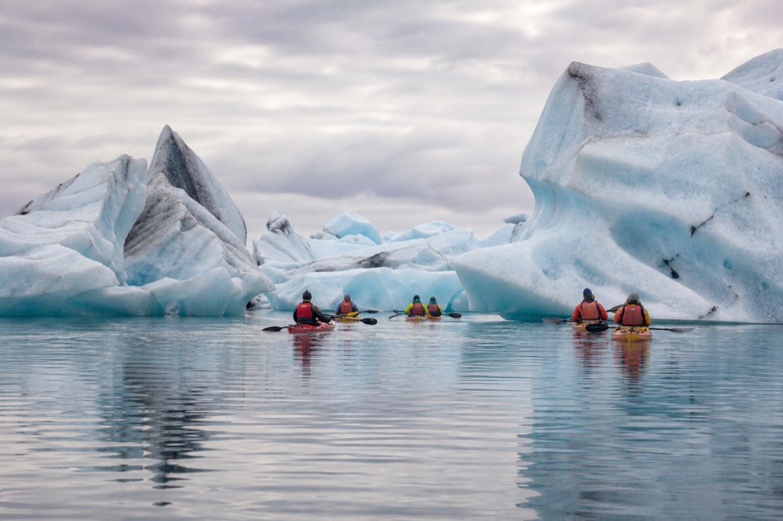 A guided kayak group paddling quietly between pale blue icebergs on the still surface of Jökulsárlón Glacier Lagoon