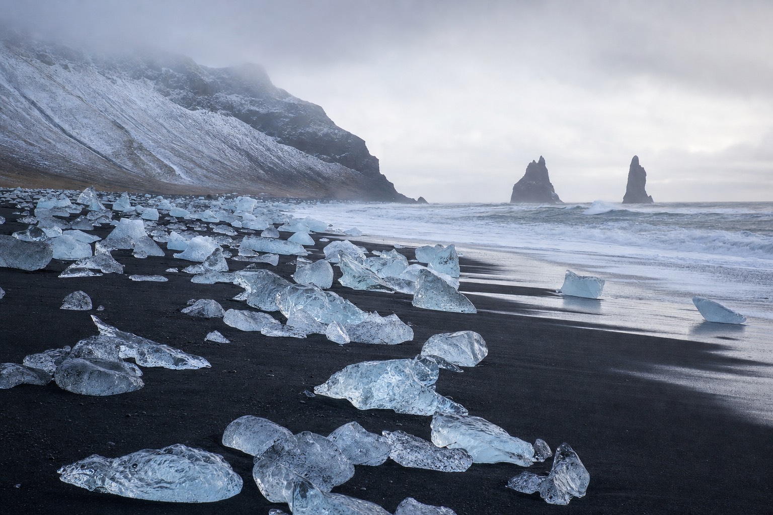 Split scene of Iceland's two black beaches, glacier ice glittering on dark sand on one side and towering basalt sea stacks on the other