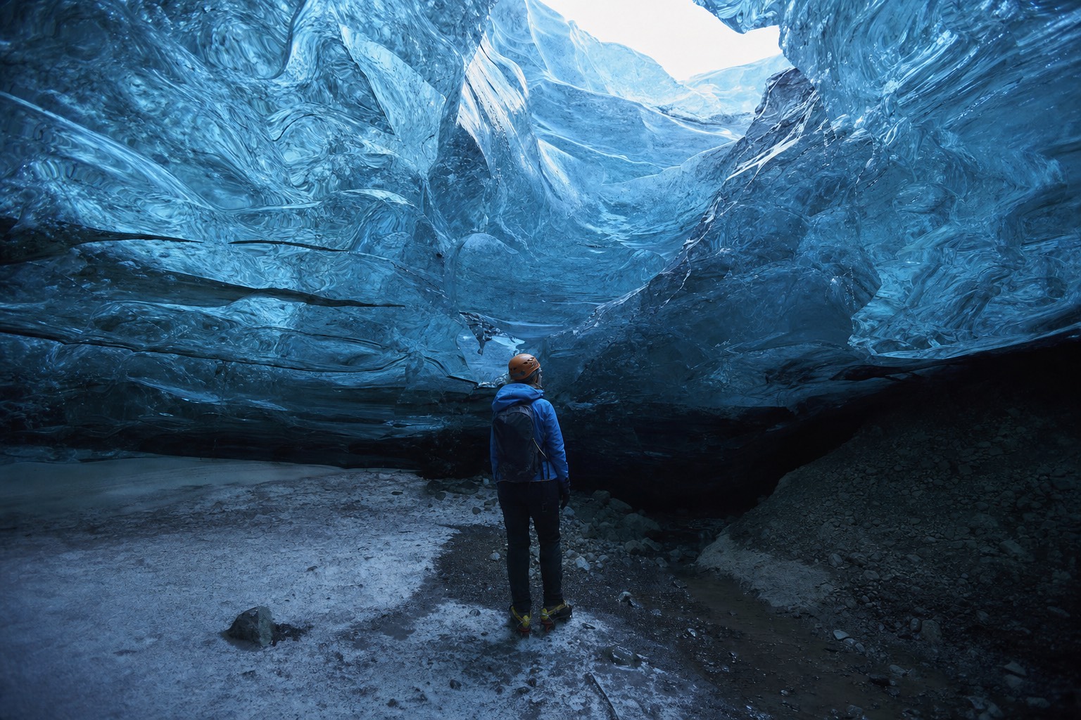 A person in crampons and a helmet standing inside a natural blue crystal ice cave under Vatnajökull, light glowing through the ice ceiling