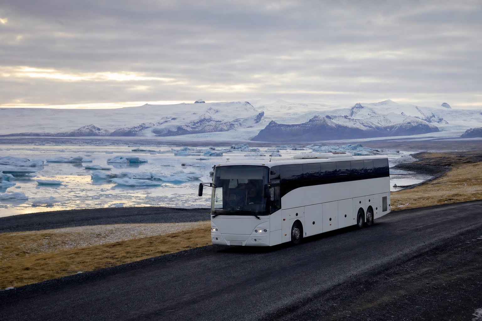 A coach on Iceland's Route 1 with the glacier lagoon and floating icebergs in the distance under low winter light