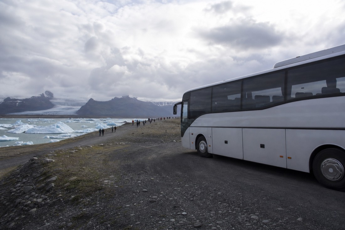 A coach parked at Jökulsárlón as day-trip visitors walk toward the iceberg-filled lagoon on Iceland's south-east coast