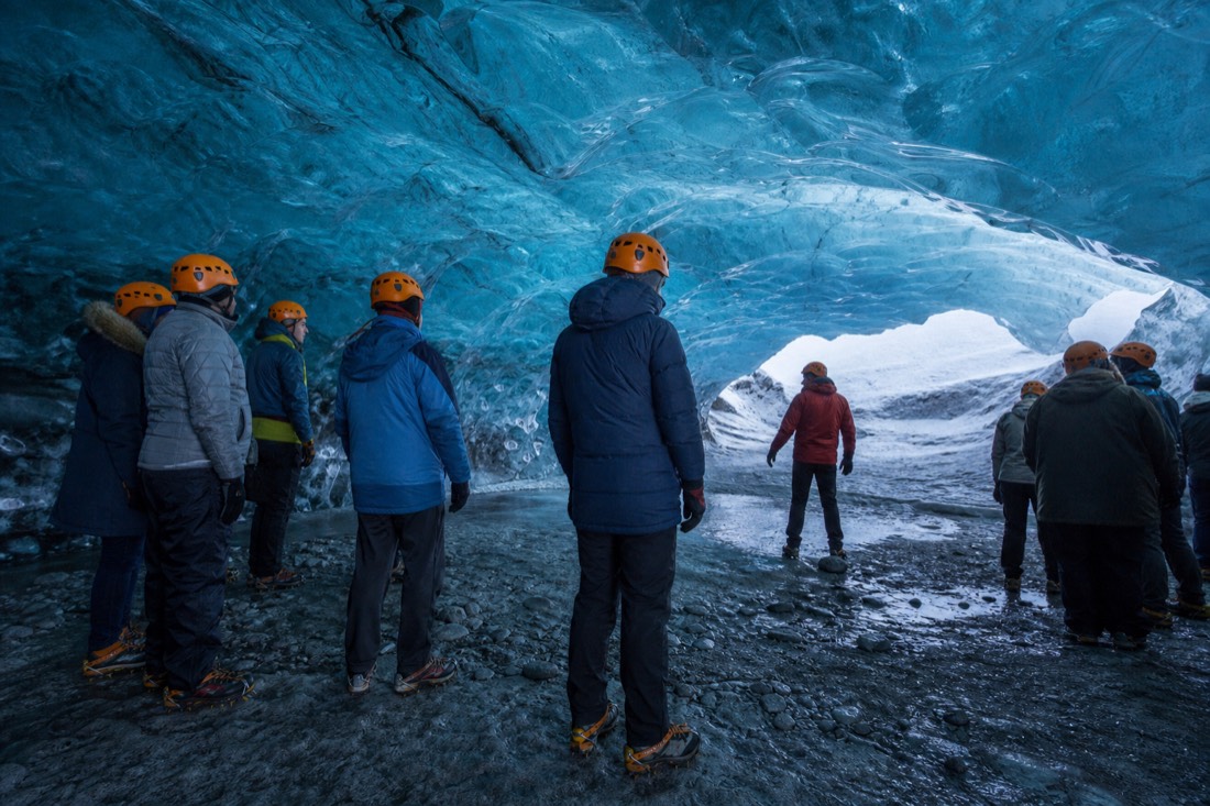 Guided visitors standing inside a blue Vatnajökull ice cave near Jökulsárlón with helmets and crampons
